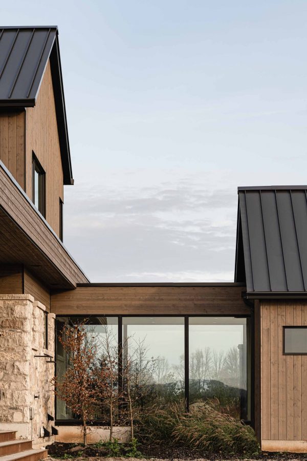 Architectural detail of a contemporary country home, featuring stone, wood and metal materials, a glass breezeway, and modern lines